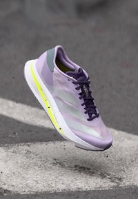 Vaalean violetti juoksukenkä, jossa on verkkomainen päällinen, hopeiset raidat ja kirkkaan keltainen pohja. Kevyt muotoilu ja virtaviivainen siluetti.
