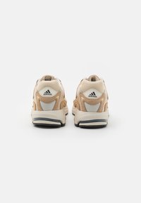 Baskets beige et crème avec panneaux en maille, semelle robuste et accents noirs. Présentent le logo Adidas sur le talon et la languette.