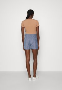 Top aderente marrone abbinato a pantaloni corti di jeans blu chiaro, con una texture liscia e un taglio classico; indossato con sneakers bianche.