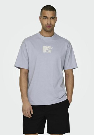 Licht lavendelkleurig katoenen t-shirt met een ronde hals en korte mouwen; heeft een wit MTV-logo op de borst. Gepaarde met zwarte shorts.