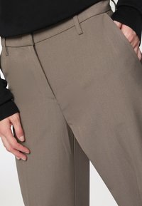 Pantaloni marroni su misura con una texture liscia, design elegante e tasche laterali; abbinati a un top nero a maniche lunghe.