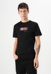 Zwarte katoenen T-shirt met een centraal rood grafisch ontwerp, korte mouwen en een ronde hals. De stof lijkt glad en zacht te zijn.