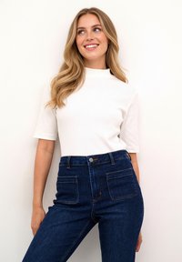 Haut blanc à manches courtes côtelé associé à un jean bleu foncé taille haute avec poches avant et une silhouette ajustée.