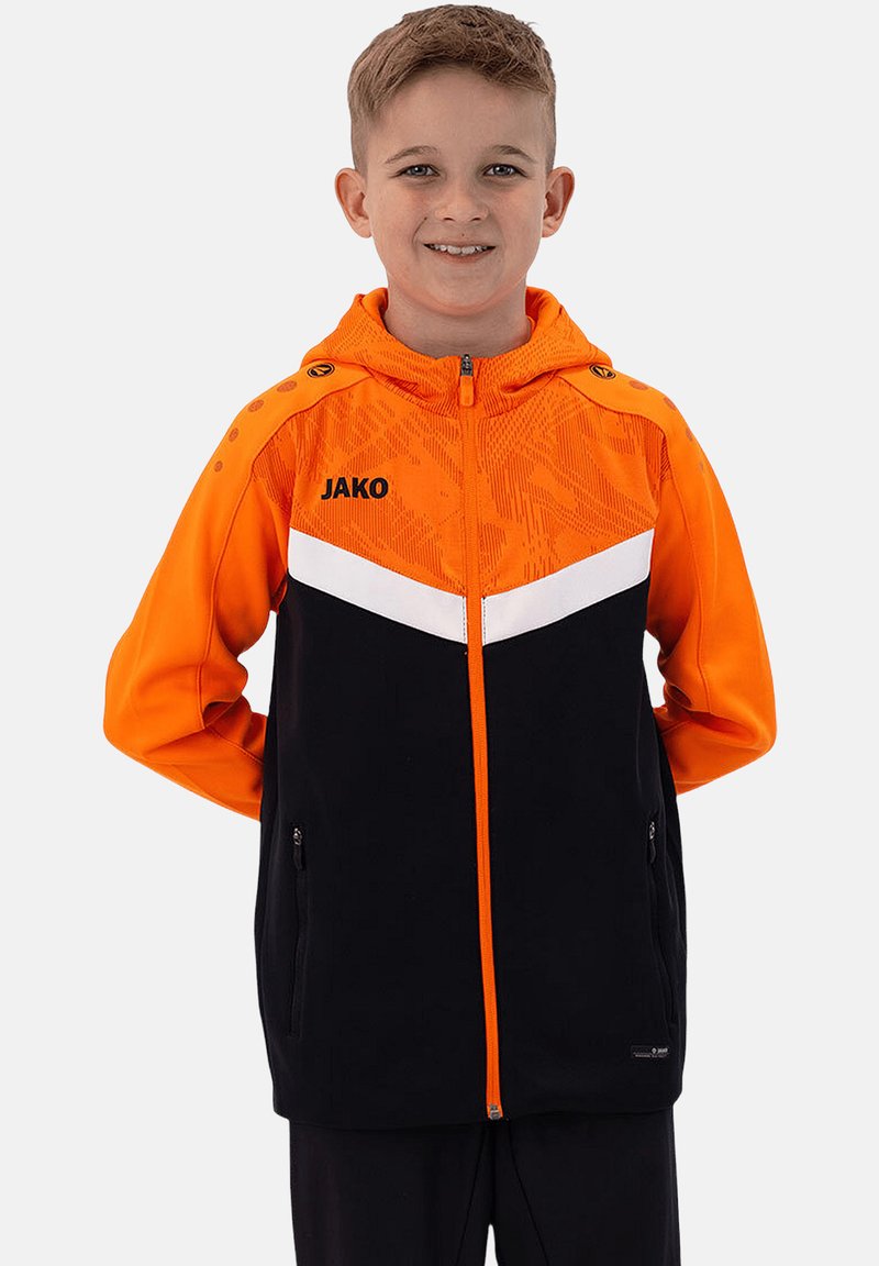 Schwarze und orange Zip-Jacke mit Kapuze, ausgestattet mit einem weißen Chevron-Design, strukturiertem Stoff und seitlichen Reißverschlusstaschen. "JAKO"-Logo auf der Vorderseite.