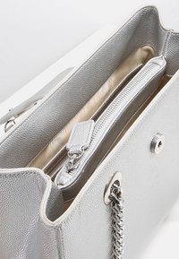 Silver textured handväska med en slät innertyg. Har ett fack med dragkedja och en axelkedja för ökad funktionalitet.