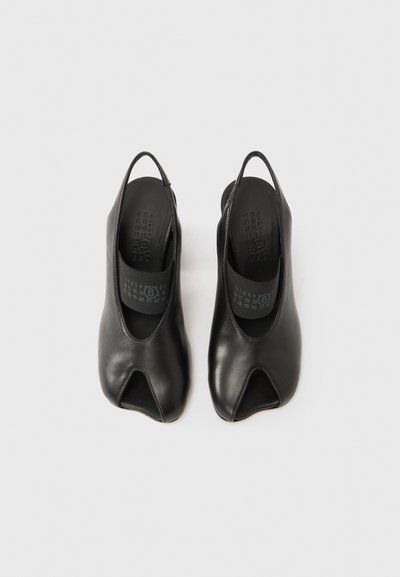 Fekete bőrből készült, nyitott orrú cipő pántos kialakítással, sima textúrával és minimalista esztétikával, jellegzetes kivágott formával.