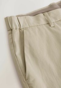 Beige Hose aus Baumwolle mit glatter Textur, flacher Vorderseite, Seitentaschen und einem einfachen Taillenbunddesign.