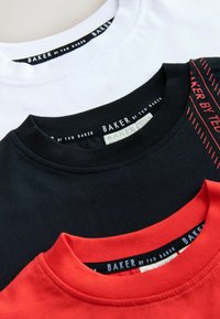 Kolm T-särki kuhjatud: üks valge, üks must punaste aktsentidega ja üks punane. Valmistatud puuvillast, ümmarguste kaelustega ja nähtavate sildimärgistega.