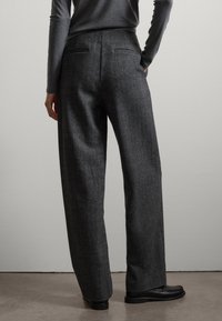 Pantalons gris à taille haute en tissu texturé ; avec des jambes droites, de subtils poches arrière et des chaussures plates noires.
