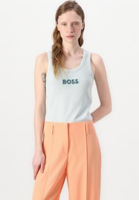 Vaaleansininen ribattutoppi, jossa on turquoise-värinen "BOSS" brodeerattuna, yhdistettynä korkeavyötäröisiin korallinvärisiin housuihin, joissa on etupinnoitteet.