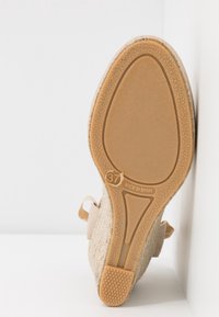 Semelle de chaussure compensée beige avec semelle en caoutchouc texturée, taille 37, et empreinte "Made in Spain", reposant contre une surface blanche.