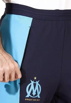 Marineblauwe en lichtblauwe sportbroeken met een zijzak met rits, voorzien van een logo en tekst in goud op het onderbeen en een gladde textuur.