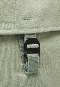 Groene stoffen rugzak met een gestructureerd oppervlak, voorzien van een zwarte plastic sluiting, gestikte accenten en een rechthoekige vorm.