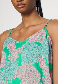 Camiseta sin mangas con estampado floral que presenta motivos en tonos rosa pastel y azul sobre un fondo verde; tirantes ajustables; tejido ligero.