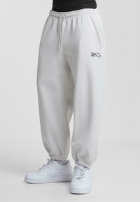 Lysegrå sweatpants med elastisk talje og manchetter, med sidelommer og et sort logo som accent. Stylet med hvide sneakers.