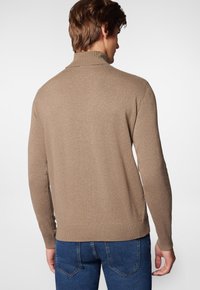 Jasnobrązowy sweter z dzianiny z wysokim kołnierzem, ściągaczami u rękawów i na dole, w połączeniu z niebieskimi dżinsami. Gładka struktura, dopasowany krój.