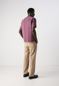 Bordová bavlněná tričko se volným střihem, kombinované s béžovými kalhotami. Černé boty dokončují outfit. Hladké textury a neutrální barevná paleta.
