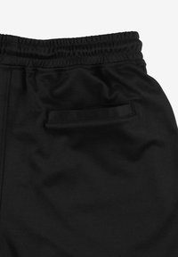 Czarne spodnie z elastycznym pasem i pojedynczą tylną kieszenią z lamówką, wykonane z gładkiej, lekko teksturowanej tkaniny.