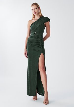 Asymmetrische groene fluwelen jurk met een zijsplit, geplooide textuur en een riemdetail. Heeft een getailleerde silhouette en een schone, elegante uitstraling.
