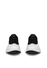 Paire de baskets noires et blanches avec des semelles blanches épaisses, vue de face sur un fond blanc.