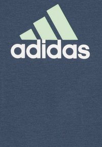 T-shirt navy con il logo Adidas in bianco e tre strisce diagonali verdi sopra, realizzato in un morbido tessuto testurizzato.