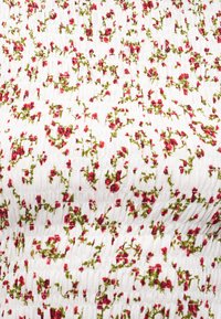 Tissu blanc texturé avec de petites fleurs rouges et des tiges feuillues vertes imprimées partout dans un motif dense et dispersé.