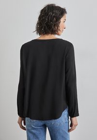 Maglietta nera a maniche lunghe con scollatura rotonda, texture liscia e vestibilità comoda. Abbinata a jeans in denim blu chiaro, con una vista posteriore sottile.