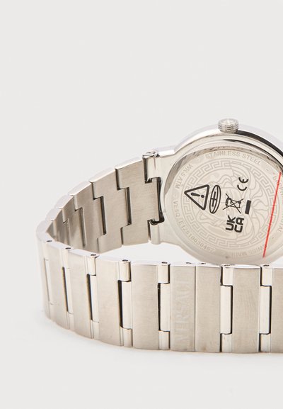 Ασημί μπρασελέ ρολογιού από ανοξείδωτο ατσάλι και πίσω κάλυμμα με χαραγμένες λεπτομέρειες της μάρκας και διάφορα σύμβολα πιστοποίησης.