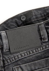 Sort justerbar knaplinning indvendigt i falmet sorte jeans med et syet rektangulært lædermærke.