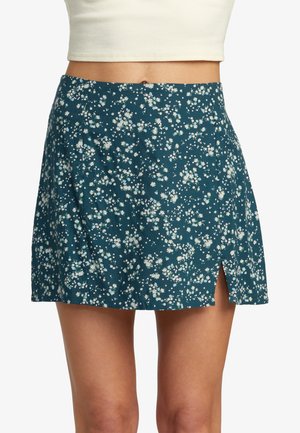 Teal mini skirt with small white floral print and front slit worn with a cream cropped ribbed top against a white background.