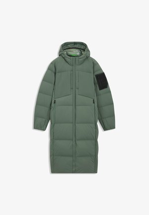 Cappotto verde lungo e gonfio realizzato in materiale sintetico, dotato di cappuccio, due tasche frontali e una tasca nera sul braccio con un dettaglio quadrato.