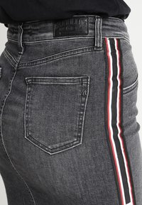 Šedé džíny s vysokým pasem a zadní kapsou, s bočním pruhovým designem v černé, červené a bílé barvě pro kontrast.