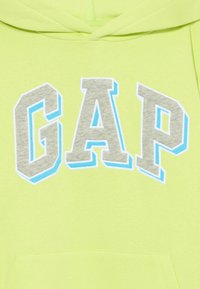 Ljus neongrön hoodie med "GAP" i grå bokstäver som är omramade med blått. Mjuk textur med en frontficka och huva.