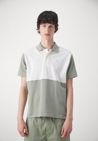 Polo tričko v khaki a bielej farbe s blokovaním farieb, vyrobené z jemnej bavlny; obsahuje golier, trojbuttonovú légu a vyšívané logo.