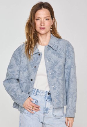 Giacca leggera blu con trama floreale, dotata di colletto, bottoni a scatto e vestibilità ampia, abbinata a jeans blu chiaro.