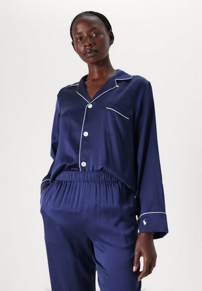 Navyblaues Satin-Pyjama-Set mit weißen Paspeln, langen Ärmeln und elastischem Bund. Mit einer Brusttasche und einem Logo am Bündchen.