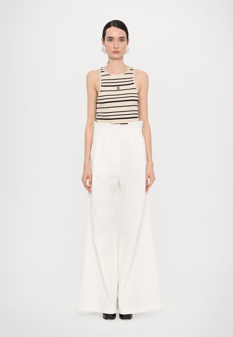 Black and beige striped sleeveless top paired with high-waisted white wide-leg trousers. Model wearing black ankle boots.