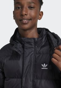Black puffer jacket with a hood, featuring a quilted design and an embroidered white Adidas logo on the chest. Smooth, shiny fabric.