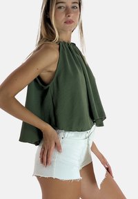 Top verde senza maniche con scollatura arricciata, tessuto fluido; abbinato a pantaloni corti in denim bianco strappati, con orli sfrangiati.