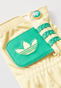 Leather glove featuring a yellow base with a green patch, embossed logo, green stitching, and decorative braiding on the wrist.