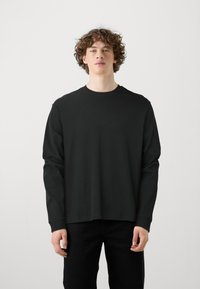 Zwarte lange mouwen T-shirt met ronde hals, gemaakt van katoen. Heeft een relaxed fit en een rechte zoom, met een eenvoudig, effen kleurontwerp.
