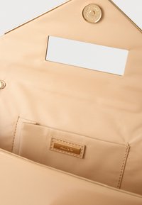 Intérieur de sac beige avec une petite poche et une fermeture à pression dorée, ornée d'une étiquette en or embossée du mot "ALDO".