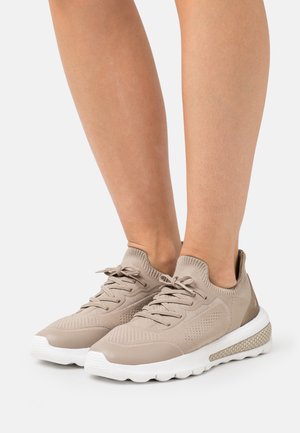 Zapatillas de punto beige con suelas de goma, diseño de cordones, patrones texturizados en los laterales y una sección de talón elevada y transparente.