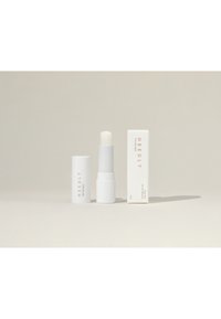 Tube de baume à lèvres blanc avec un dessus arrondi à côté d'une élégante boîte blanche, tous deux présentant un texte minimal en couleurs sombres et claires.