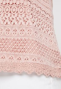 Světle růžová háčkovaná tkanina s různými složitými vzory a texturami, s krajkovým zdobením na lemu.