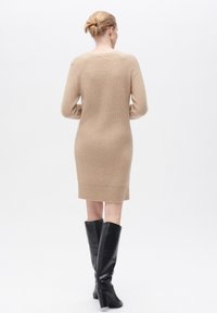 Abito in maglia color beige con orlo a coste, dotato di maniche lunghe e scollatura rotonda, abbinato a stivali neri fino al ginocchio.