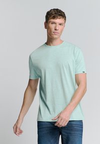Licht muntgroene t-shirt met korte mouwen gemaakt van zachte stof, met een ronde hals en subtiele textuur; gecombineerd met donkerblauwe jeans.