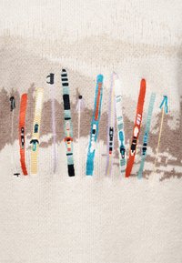 Χρωματιστός κεντητός εξοπλισμός σκι, περιλαμβάνοντας σκι και μπαστούνια, σε φόν από μπεζ πλεκτό ύφασμα.