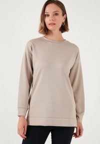 Felpa beige chiaro con scollatura rotonda, maniche lunghe e vestibilità comoda. Presenta una trama liscia e polsini e orlo a costine.