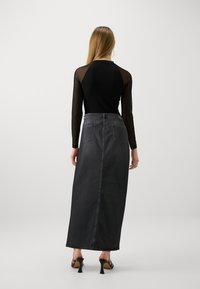 Black long-sleeve top with sheer sleeves, paired with a high-waisted dark grey denim maxi skirt featuring a straight cut and back pockets.